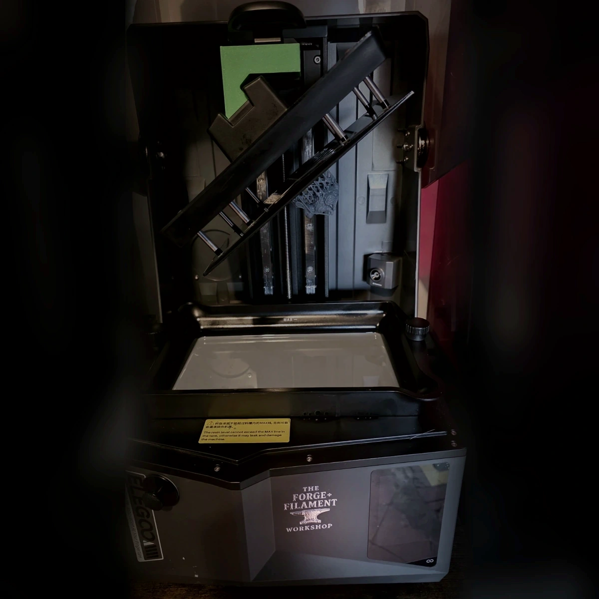 A genuine square workshop photograph showing a resin printer, the slanted build plate draining above the vat and the Forge and Filament Workshop logo on the front of the printer