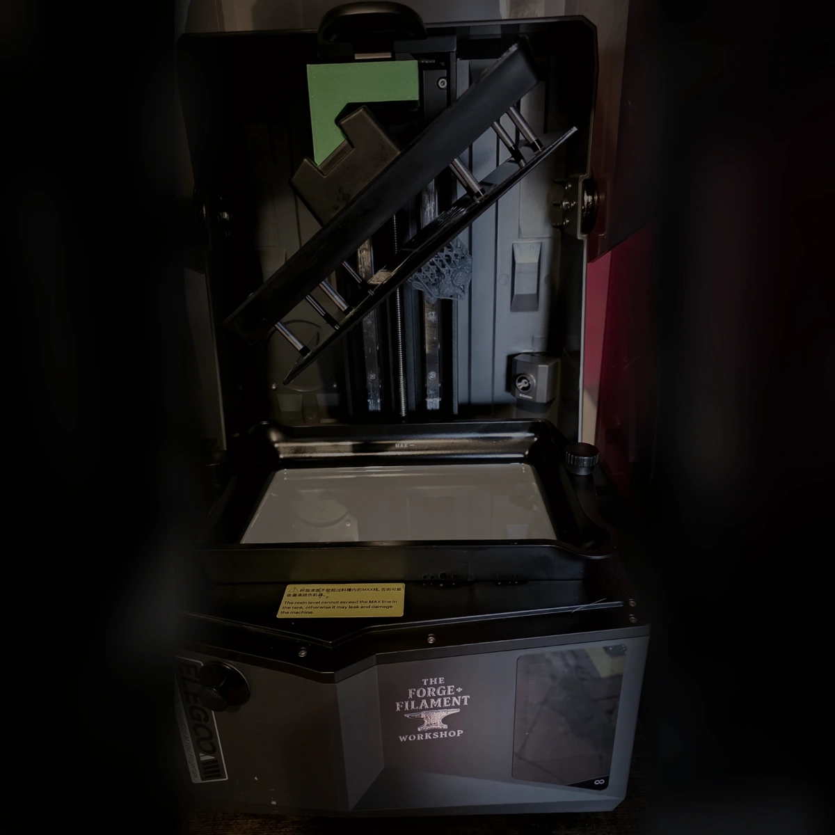 A genuine square workshop photograph showing a resin printer, the slanted build plate draining above the vat and the Forge and Filament Workshop logo on the front of the printer